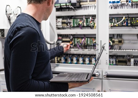 Caucasian Male Superyacht Engineer - ETO working on the engine room control panel with laptop