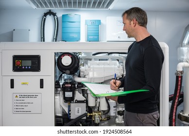 Caucasian Male Superyacht Engineer working on the engine room, inspecting the generator with checklist folder and pen in his hand