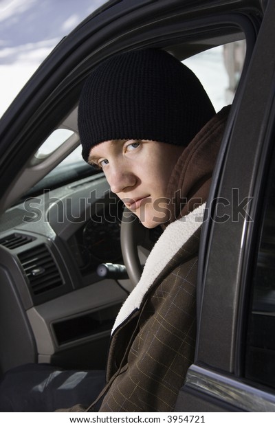 Caucasian male teenager sitting in car looking\
back at viewer.