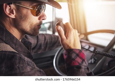 Caucasian Male Truck Driver Sitting In Cab Of Vehicle Talking On Two Way Radio. 