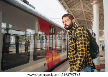 caucasian man with backpack standing at platform going to take train. 