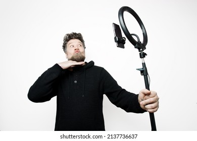 Caucasian Man With Beard And Lips In A Kissing Pose Holding A Light Ring With A Parallel Light And A Mobile Phone On A White Background