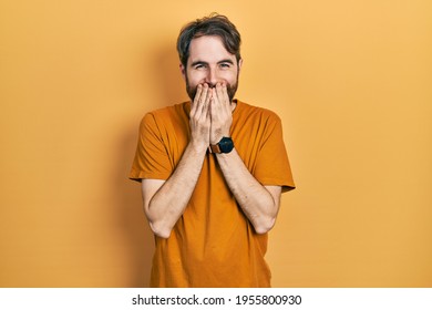 Caucasian Man With Beard Wearing Casual Yellow T Shirt Laughing And Embarrassed Giggle Covering Mouth With Hands, Gossip And Scandal Concept 