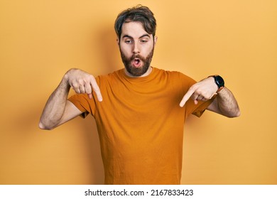 Caucasian Man With Beard Wearing Casual Yellow T Shirt Pointing Down With Fingers Showing Advertisement, Surprised Face And Open Mouth 