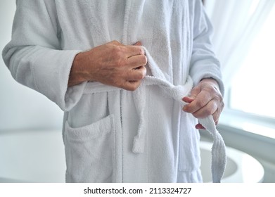 Caucasian man belting the white terry bathrobe
