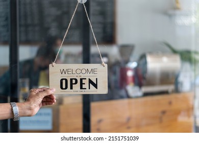Caucasian man changes sign from closed to open at the entrance of his small coffee shop. Small business food and drink concept. - Shutterstock ID 2151751039