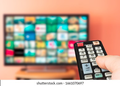 Caucasian Man Choosing What To Watch On TV At Home. Video On Demand Or VOD Abstract Concept. Changing Channels And Adjusting Volume With Television Remote Control. 