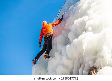 Caucasian man with climbing equipment hiking at a frozen waterfall, taking a break 