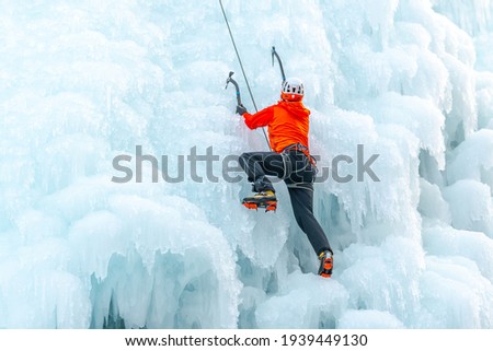 Caucasian man with climbing equipment, ice axes and rope, hiking at a frozen waterfall