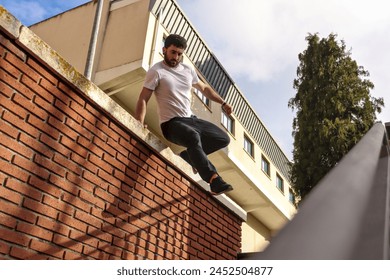 Caucasian man doing parkour coming down from a wall, prepared to fall to the ground in an urban environment - Powered by Shutterstock