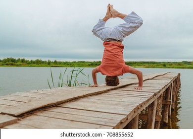 Caucasian Man Doing Upside Down Yoga On Pier At Lake