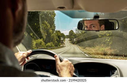 Caucasian Man Driving A Car. View Of The Countryside Road From The Windshield (front Window) Of The Vehicle. Face Reflection In The Rear-view Mirror.