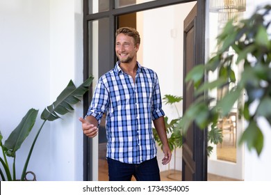 Caucasian Man Enjoying His Time At Home, Standing At His Open Front Door, Greeting A Visitor, Looking Away From The Camera And Smiling