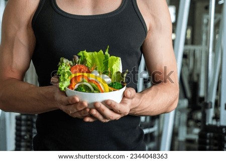 Caucasian man exercising muscle building holding wooden bowl of vegetable salad healthy eating in gym