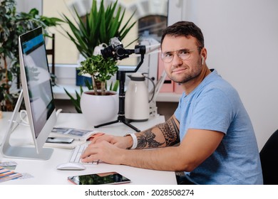 Caucasian Man With Glasses Poses Sitting At Table With Computer In Office