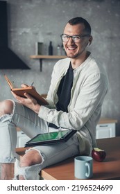 Caucasian Man Having Coffee In The Morning At Kitchen Working With A Tablet PC And Writing In An Open Notepad. Distance Education. Education Business Concept