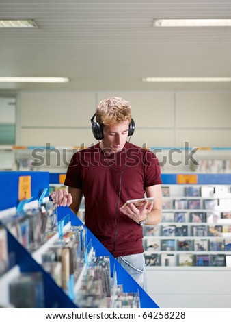 caucasian man with headphones, choosing cd in music shop. Vertical shape, front view, waist up, copy space