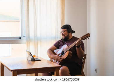 Caucasian man, heavyset with a large beard, glasses and a cap. Receiving an online guitar lesson on your tablet. - Powered by Shutterstock