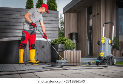 Caucasian Man in His 40s Pressure Washing Concrete Bricks Patio Using Surface Attachment. Modern Garden Shed and a Hot Tub in a Background. - Shutterstock ID 2312886143
