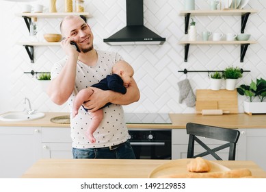 A Caucasian Man Holding A Baby While Talking On Phone In The Kitchen 