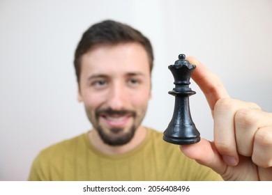 Caucasian Man Holding Black Queen Chess Piece Between Fingers