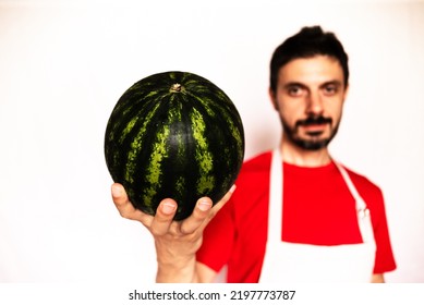 Caucasian man holds a watermelon in his hand. Healthy food for diet, man with red t-shirt on out of focus white background.