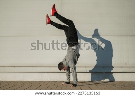 Caucasian man in hooded sweatshirt doing handstand outdoors. 