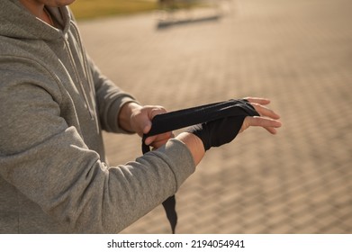 Caucasian Man In Hoodie Bandaging His Hands Before Boxing Class Outdoors.