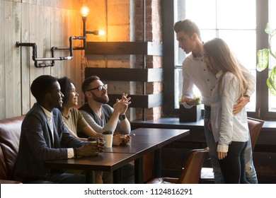 Caucasian Man Introducing Girlfriend To Multiracial Millennial Friends Sitting At Table, Enjoying Coffee In Cafe, Male Worker Acquainting Colleagues With New Female Employee At Meeting In Coffeeshop