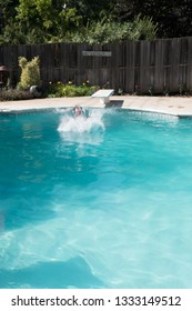 Caucasian Man Jumping Into An Outdoor Swimming Pool In The Summer. Jumping Off Diving Board Doing Cannon Ball Into A Pool With Big Splash As He Lands In The Water Of An Outdoor Pool.