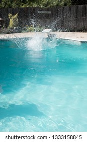 Caucasian Man Jumping Into An Outdoor Swimming Pool In The Summer. Man Lands In Pool From Jumping Off Diving Board Doing Cannon Ball Into A Pool With Big Splash As He Lands In The Pool.