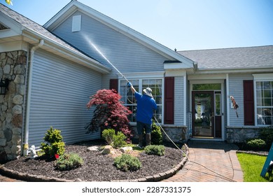 A caucasian man with a latex holding water sprayer wand power washing the siding of a house - Shutterstock ID 2287331375