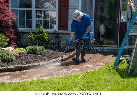 A caucasian man with a latex holding water sprayer wand power washing the brick walkway to a house