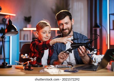 Caucasian man and little boy repairing modern quadcopter while sitting at table. Happy satisfied father teaching son different man's work at home. Parenting concept.