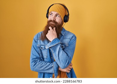 Caucasian man with long beard listening to music using headphones looking confident at the camera smiling with crossed arms and hand raised on chin. thinking positive.  - Powered by Shutterstock