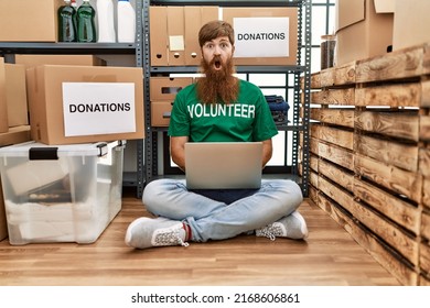 Caucasian Man With Long Beard Wearing Volunteer T Shirt Using Laptop Scared And Amazed With Open Mouth For Surprise, Disbelief Face 