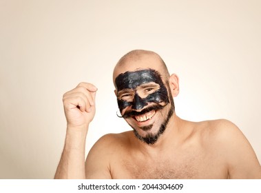 Caucasian Man Looks At Smiling Camera With Black Face Mask On His Face. Bald Adult With Mustache Concept Health And Wellness, Skin Care.