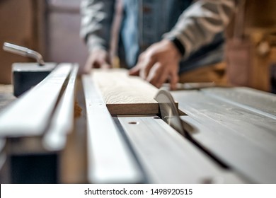 Caucasian man making wooden parts for custom furniture on machine tool called thickness planer in carpentry. Producing lumber concept