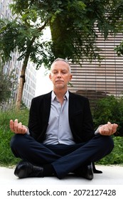 Caucasian Man Meditating In City Park Near Business Buildings. Vertical Image.