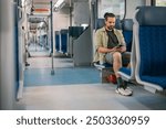 A Caucasian man with a phone rides on the train, in the skytrain, in the subway. Urban transport.  A young guy uses a smartphone in a modern train carriage during the day.