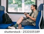 A Caucasian man with a phone rides on the train, in the skytrain, in the subway. Urban transport.  A young guy uses a smartphone in a modern train carriage during the day.