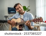 Caucasian man play guitar and produce electronic soundtrack at home. Attractive male artist musician composing, create new song using musical instrument and audio equipment in recording music studio.