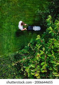 Caucasian Man Pushing Lawn Mower For Cutting Green Grass In Garden At Summer Season. Aerial View.