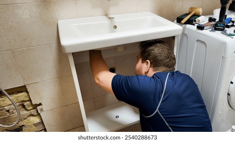 A Caucasian man repairs a bathroom sink, illustrating home improvement and plumbing maintenance challenges - Powered by Shutterstock