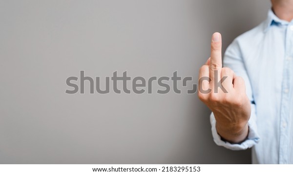 Caucasian man in shirt shows an obscene\
gesture, middle finger of hand rude sign on gray background, copy\
space. Close-up, banner with empty space for\
text.