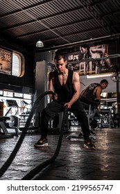 Caucasian Man With Short Hair Dressed In A Black Sweatpants And A Black Sleeveless Shirt. Man In Sports Rpa Training With Ropes.