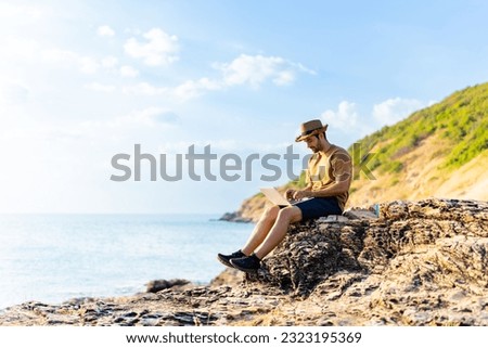Caucasian man sitting on coastline hill and working on laptop computer with drinking coffee. Handsome guy enjoy outdoor lifestyle travel ocean on summer vacation. Digital nomad and solo travel concept