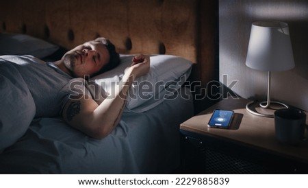 Caucasian Man Sleeps through Smartphone Alarm Clock Showing Eight in the Morning. Tired Person Oversleeping. Person and Mobile Phone Close-up. Bedside Nightstand Bedroom Apartment