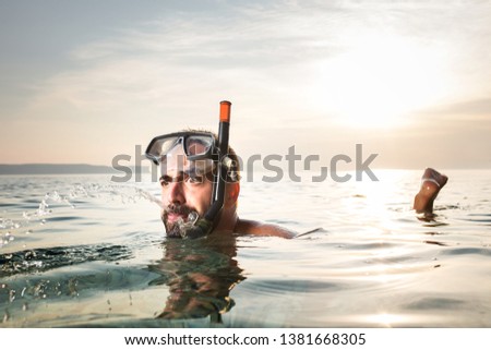 Caucasian man snorkelling,floating on the surface,spitting out water with a funny goofy facial expression,summer seaside vacation activity,cancelled due to Coronavirus COVID-19 global pandemic crisis