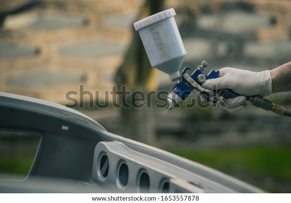 Caucasian man is spraying color with a\
compressed air paint gun on the vintage car as a restoration\
project. Man wearing protective equipment such as mask and gloves,\
professional automotive\
painter.